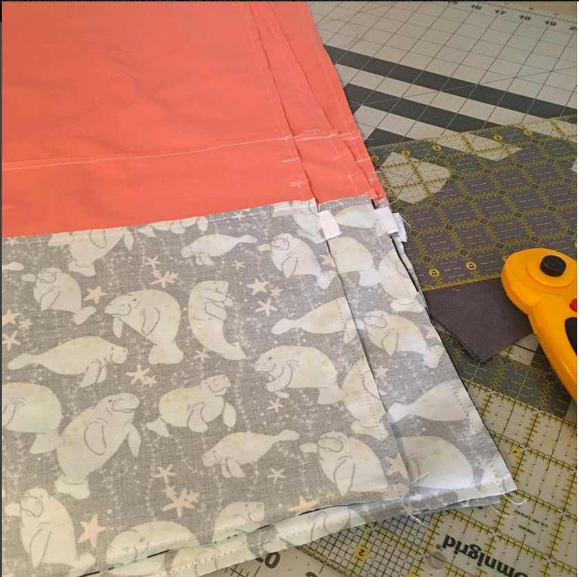 Stack of drawstring bags inside out half-sewn with coral fabric and rotary cutter